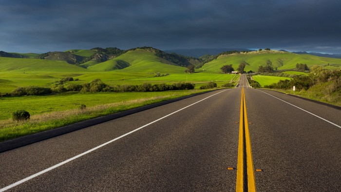 Road through green rolling hills under dark clouds