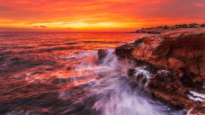 Sunset over rocky coast with crashing waves