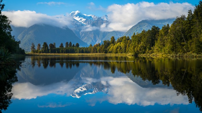 Snow-capped mountains reflected in a calm lake with trees