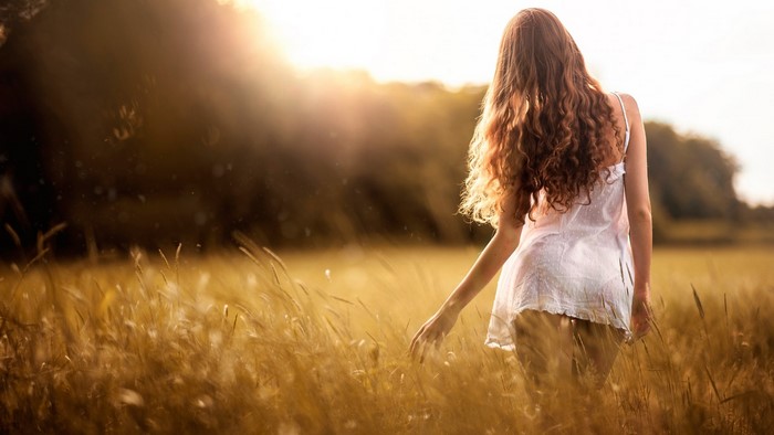 Woman walking through a field at sunset
