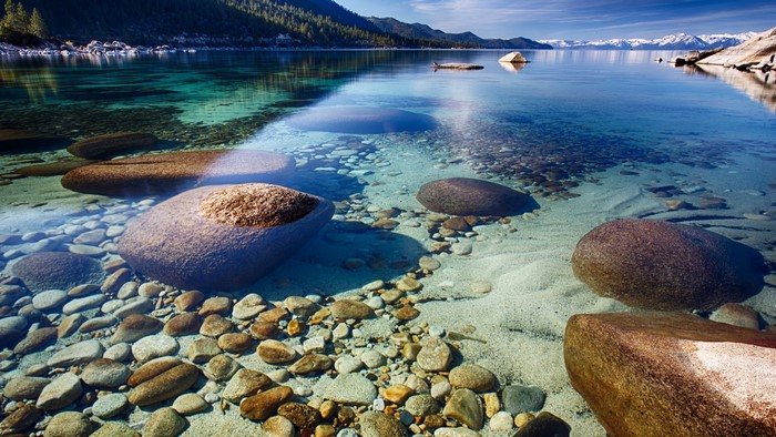 Crystal clear lake with submerged rocks and distant mountains