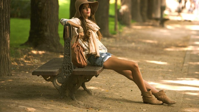 Woman in hat and shorts sitting on a park bench