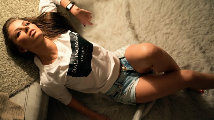 Girl in Balenciaga shirt and denim shorts lying on rug