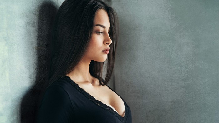 Young woman in black top leaning against wall