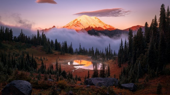 Mountain peak illuminated by sunrise over misty forest and lake