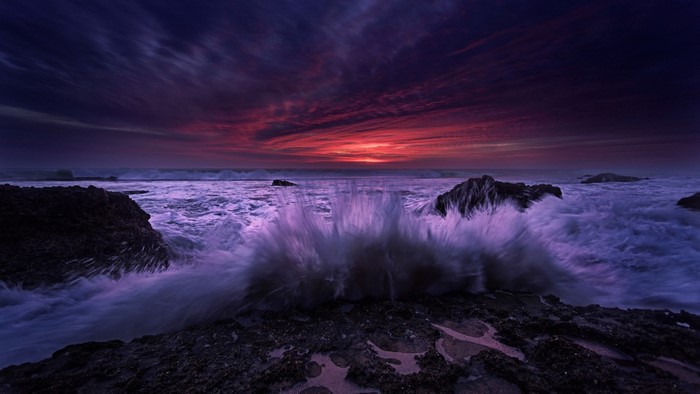 Dramatic sunset over ocean waves crashing on rocks
