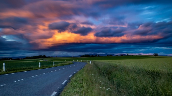 Road through fields at sunset with dramatic clouds