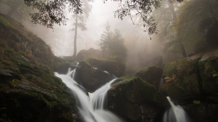 Misty forest waterfall with mossy rocks