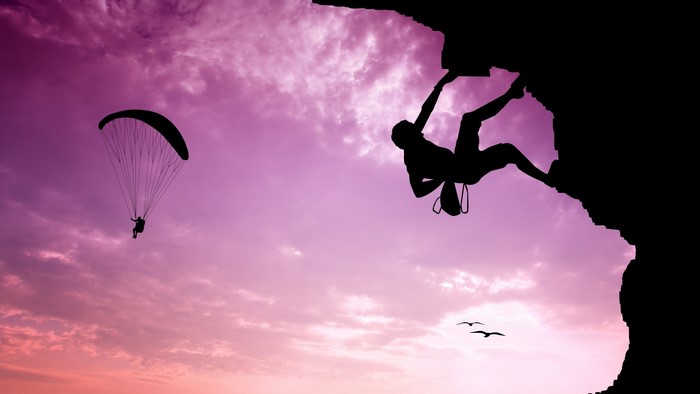Silhouette of a rock climber and paraglider at sunset
