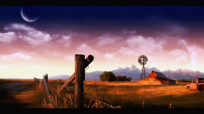 Rural landscape with barn, windmill, and mountains at sunset