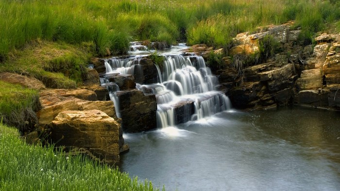 Waterfall cascading over rocks in a grassy landscape