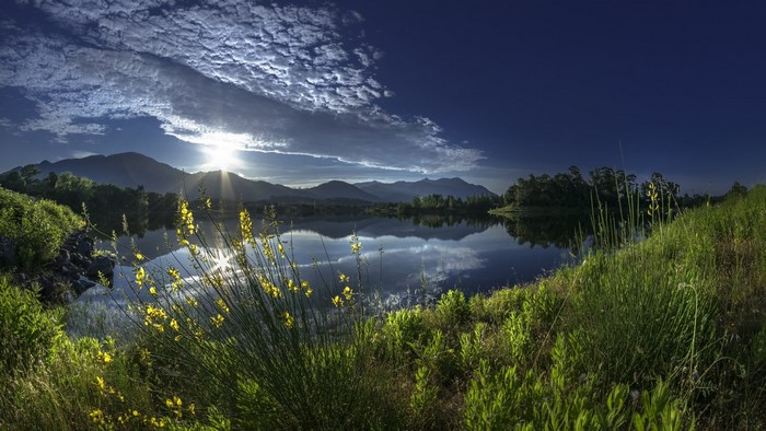 Sunrise over a calm lake with mountains and clouds
