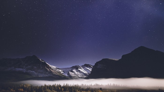Starry night sky over misty mountains and forest