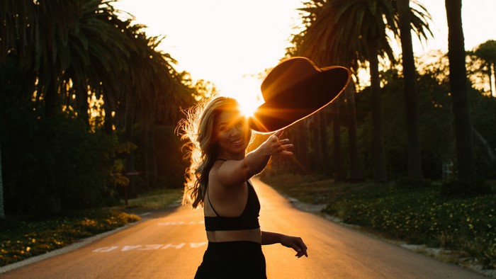 Woman in black outfit throwing hat at sunset