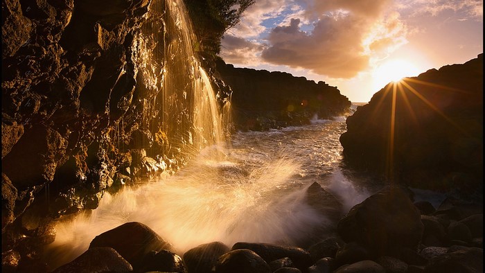 Sunset over rocky coast with waterfall and waves