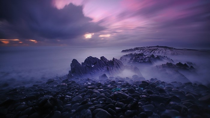 Rocky shore with purple clouds at dusk