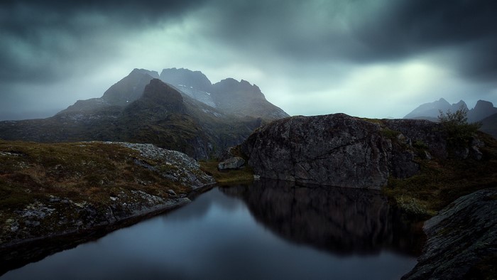 Lake reflecting mountains under stormy sky