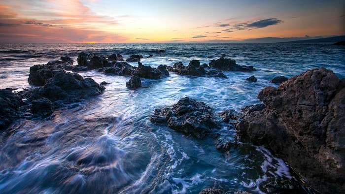 Ocean waves crashing on rocky shore at sunset