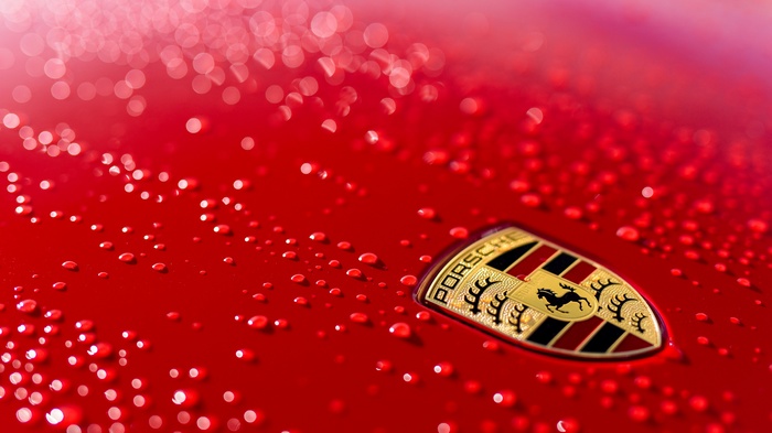 Porsche logo on a red car with water droplets