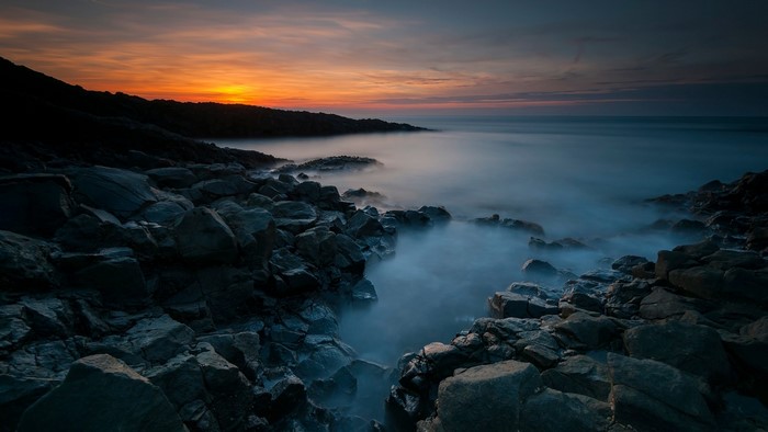Rocky shore at sunset with misty ocean