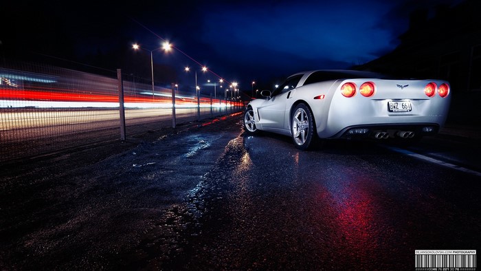 Silver Corvette parked on wet road at night