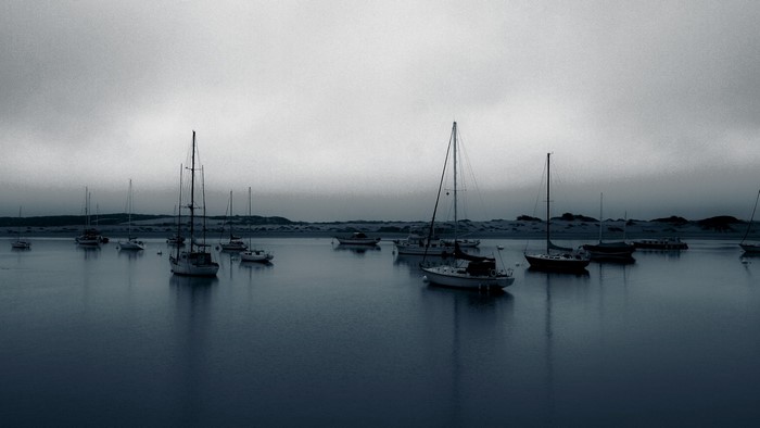 Sailboats moored in a calm bay under a cloudy sky