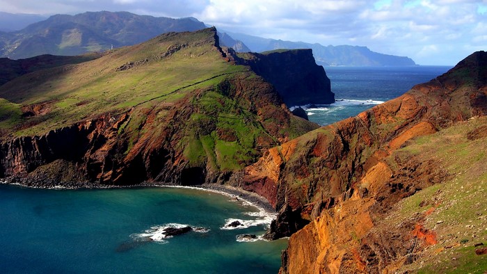 Green and red cliffs meet the blue sea