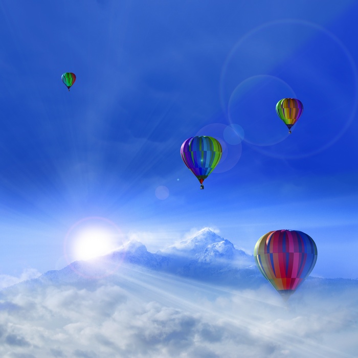 Hot air balloons over snowy mountains under a sunny sky