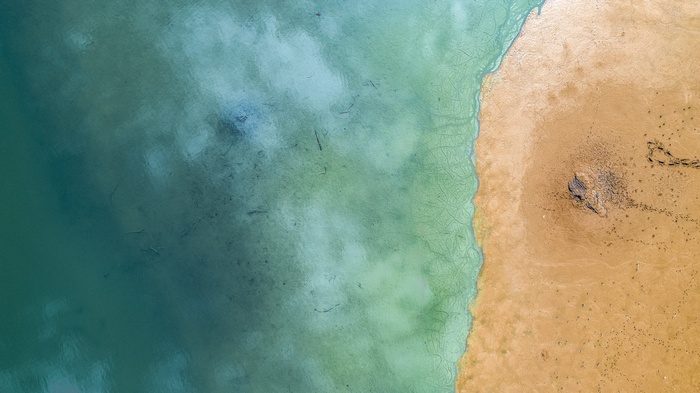 Aerial view of a sandy beach meeting turquoise water