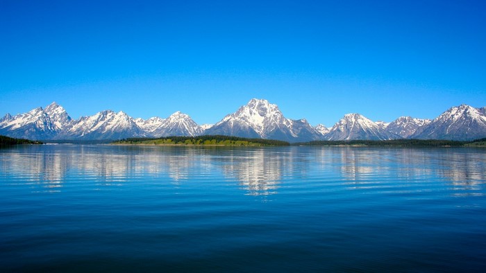 Snow-capped mountains reflected in a lake under a clear blue sky