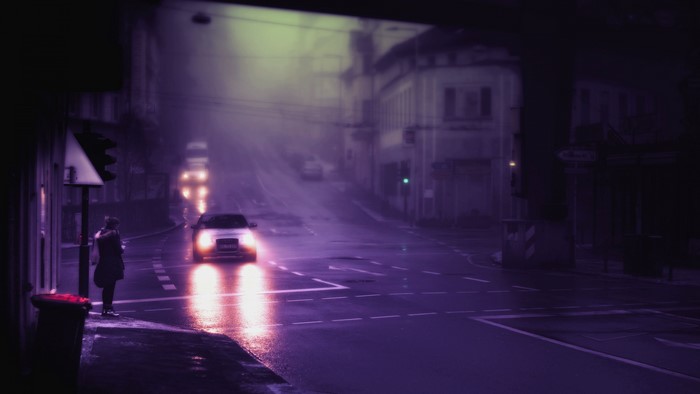 Car driving through foggy city street at night
