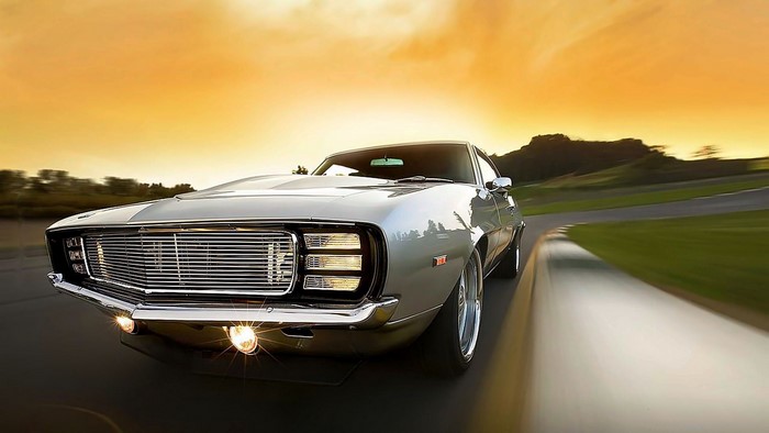 Silver 1969 Chevrolet Camaro driving at sunset