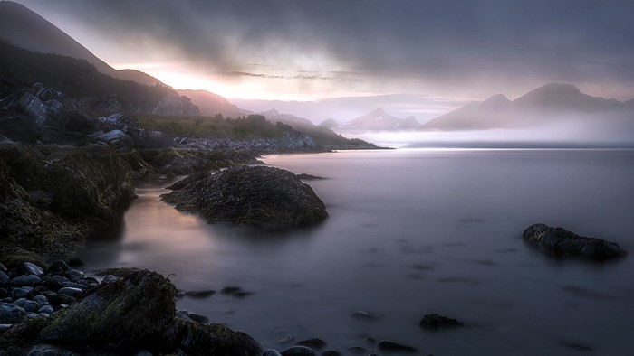 Misty mountains and rocky shore at sunrise