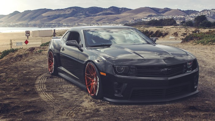 Black Chevrolet Camaro with red rims on a beach