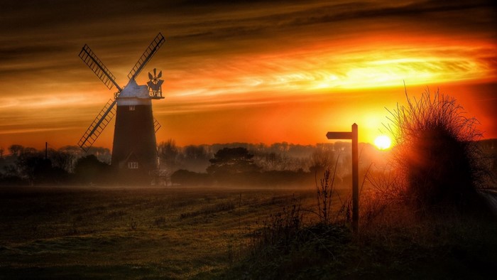 Windmill at sunrise with a signpost