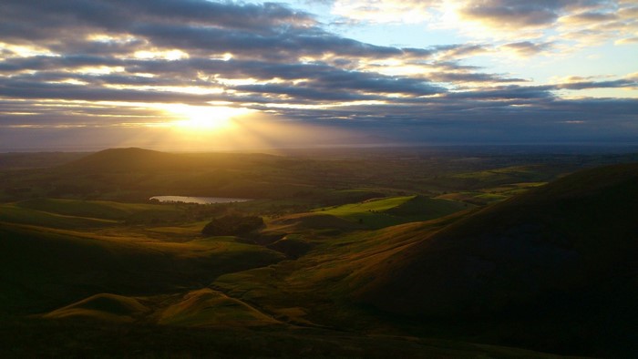 Sunset over rolling green hills and a lake