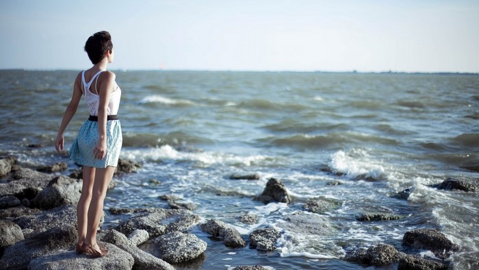 Girl on rocky shore looking at the sea
