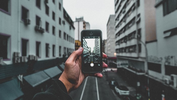 Person holding a smartphone taking a picture of a city street