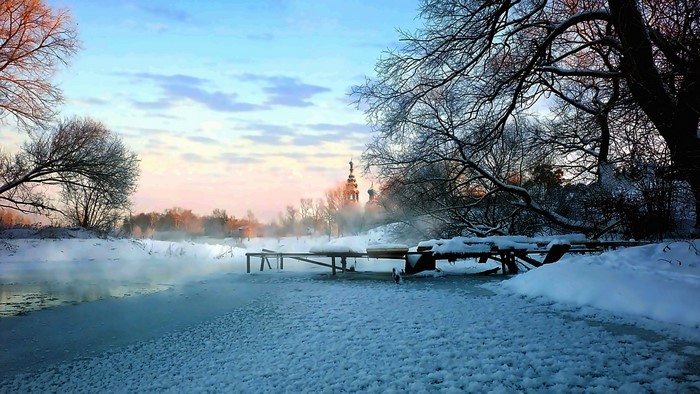 Winter sunrise over a frozen river with a temple in the background