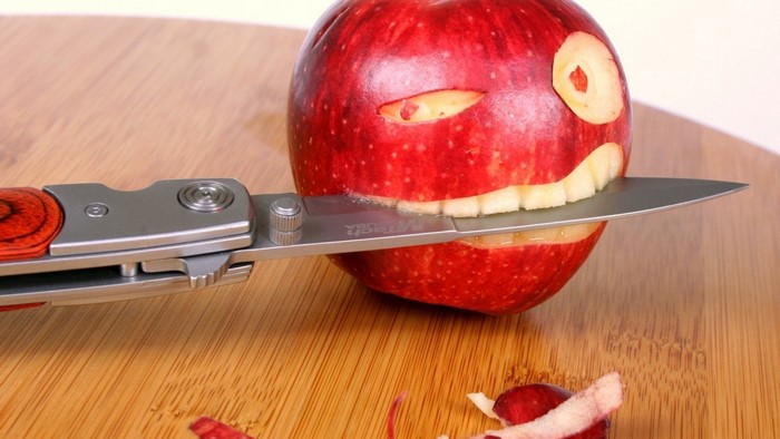 Knife cutting a carved apple on a wooden board