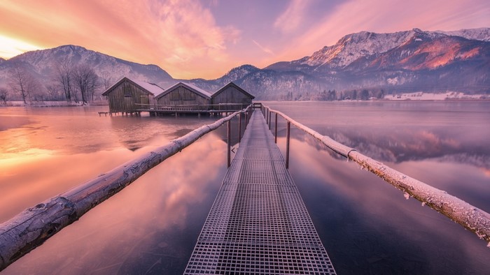 Wooden boathouses on a frozen lake with mountains at sunrise