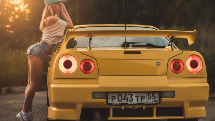 Woman in denim shorts leaning on yellow Nissan Skyline