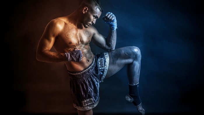 Boxer with tattoos performing a Muay Thai knee strike