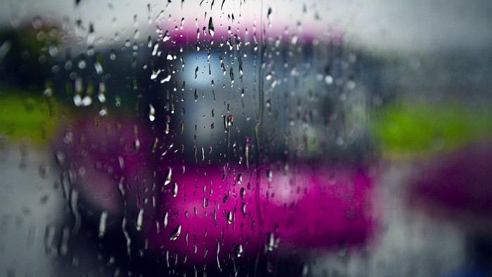 Raindrops on a window with a blurred pink vehicle