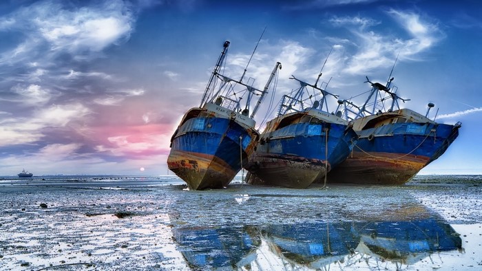 Three abandoned fishing boats on a muddy shore at sunset