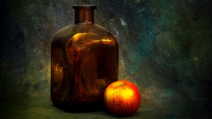 Old amber bottle and apple on textured background