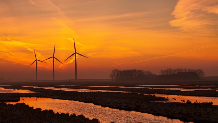 Wind turbines at sunset over water and farmland