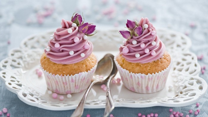 Two pink frosted cupcakes with roses and pearls
