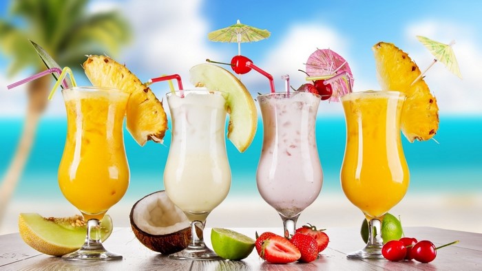 Four tropical drinks with fruit garnishes on a beach background