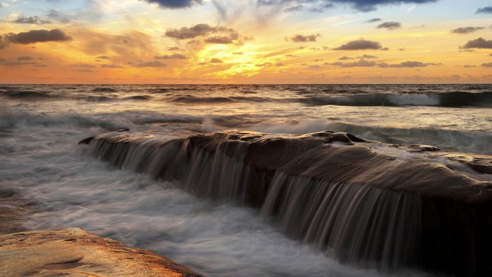 Ocean waves crashing over rocks at sunset
